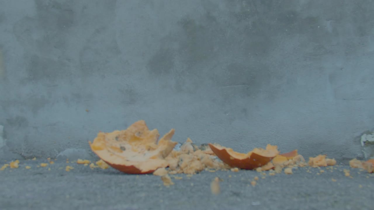 Halloween pumpkin is smashed into pieces in slow motion after being dropped onto ground