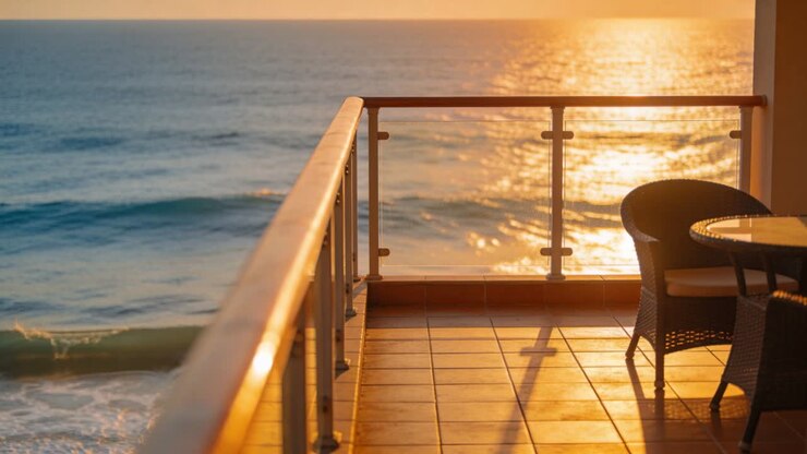 La luce del sole cangiante proietta lunghe ombre dorate su una terrazza con ringhiera, sedie in vimini e onde.