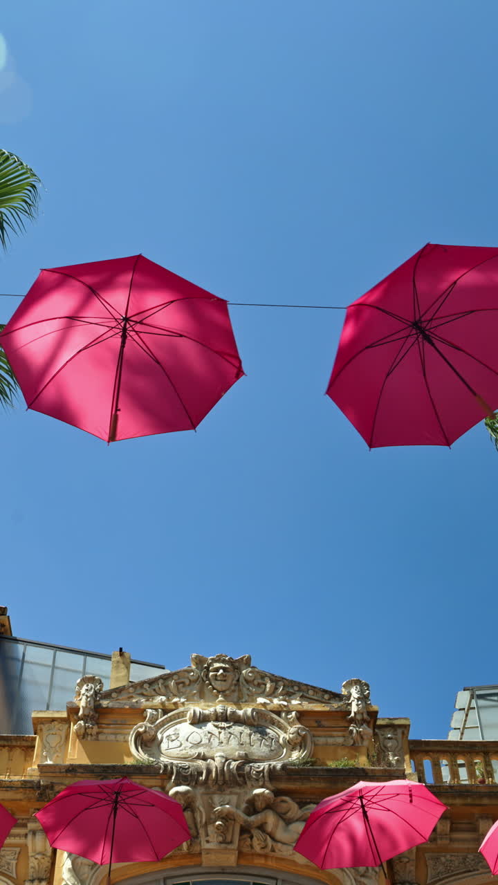 Rows of pink umbrellas above the streets of the old town in Grasse, France with the blue sky on the background. Vertical