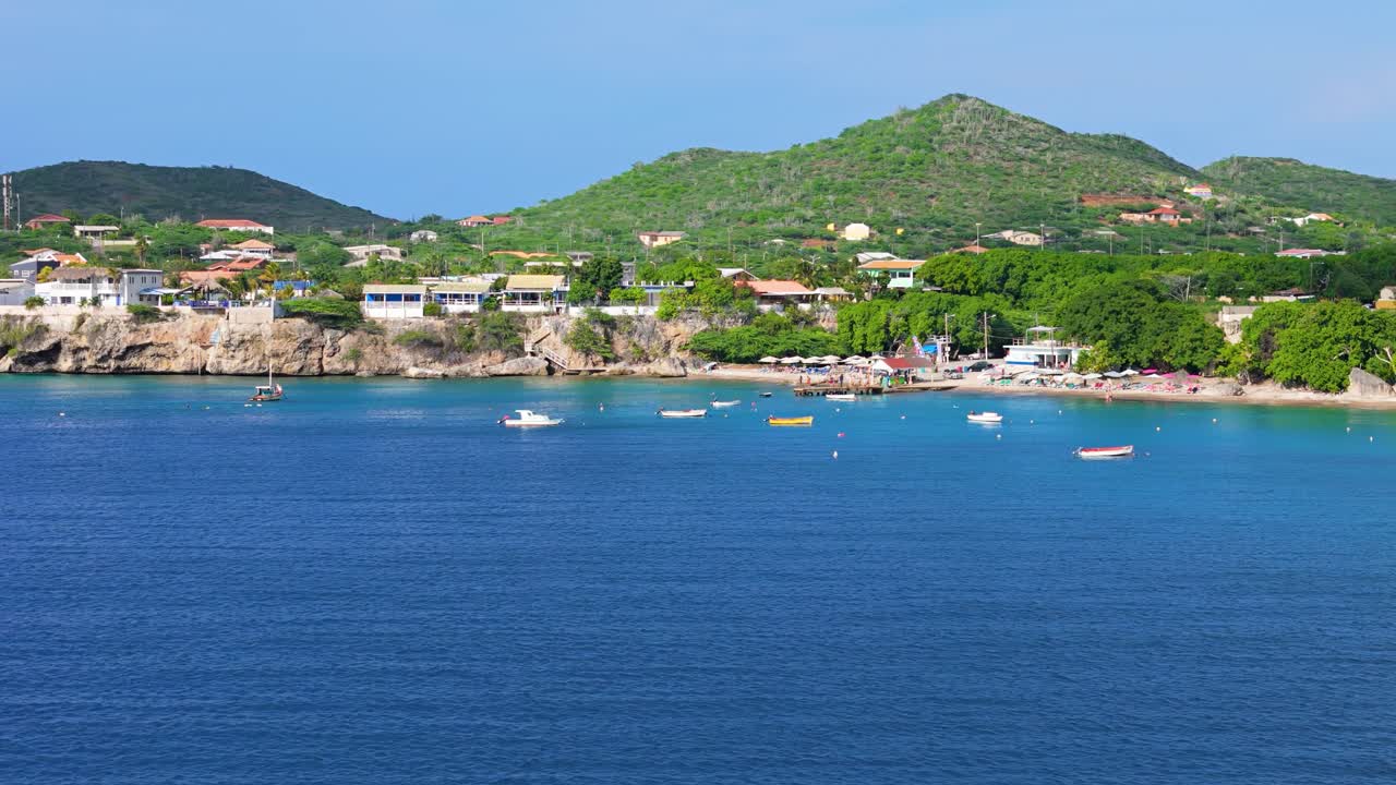 Drone orbit around coastline and Playa Piskado with boats anchored near shore on sunny day in Curacao
