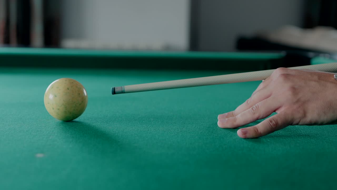 Primo piano di una mano che punta una stecca da biliardo a una palla su un tavolo da biliardo verde.