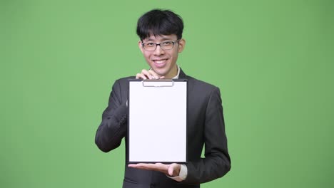 young happy asian businessman smiling while showing clipboard to camera