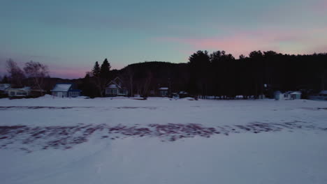 Fliegende-Drohne-Filmt-Strandhäuser-An-Einem-Zugefrorenen-See-Im-Winter-In-Kanada