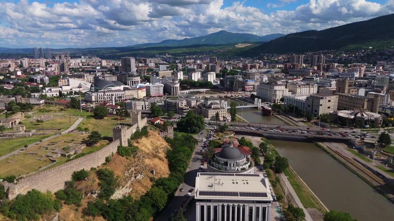 Ampia veduta aerea con drone del paesaggio urbano di Skopje che fiancheggia il letto del fiume Vardar. Sviluppo metropolitano e quartieri residenziali urbani nella capitale della Macedonia del Nord.