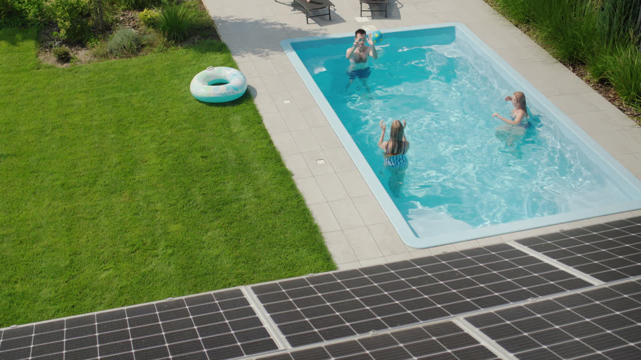 En glad familie leger i poolen, i forgrunden er der solcellepaneler på taget af deres hus