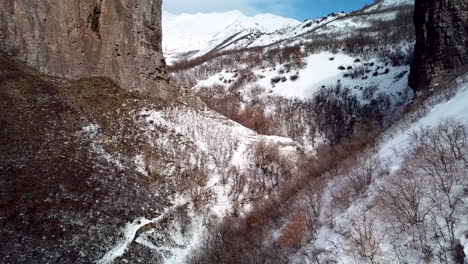 Flying-backwards-to-reveal-rugged-terrain-with-hiking-trails-below-in-winter