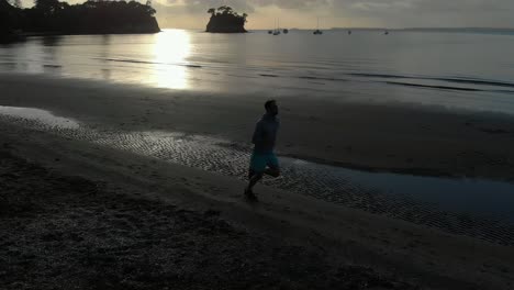 Luftaufnahme-Eines-Silhouettierten-Jungen-Mannes,-Der-An-Einem-Strand-In-Auckland,-Neuseeland,-Läuft