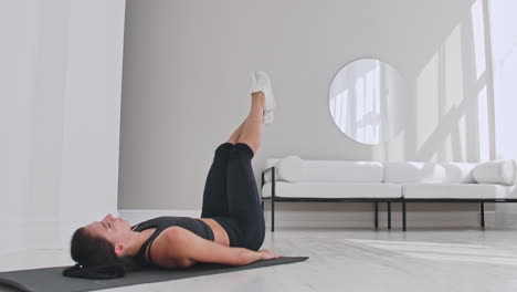 Deportista-Entrenando-En-Casa.-Atleta-Femenina-En-Forma-Haciendo-Ejercicio-Con-Un-Solo-Brazo-Tocando-El-Dedo-Del-Pie-Tumbado-En-El-Suelo-En-Un-Apartamento-Blanco.