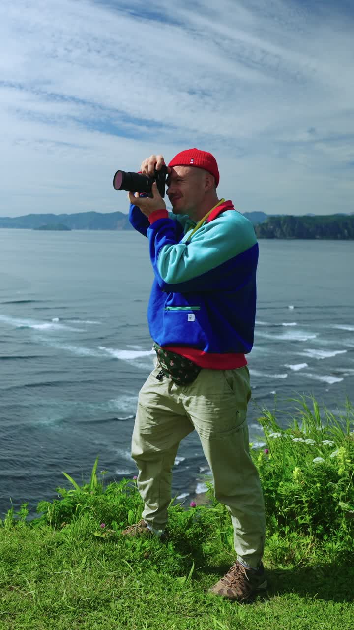 Man Taking Photo of Scenic Ocean and Mountains from Grassy Cliff