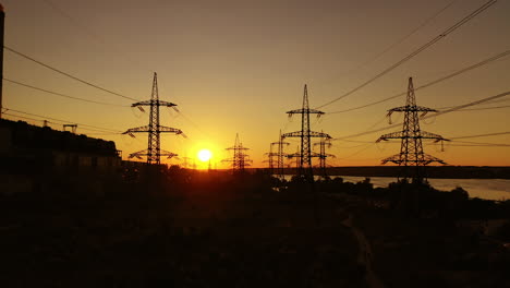 high voltage station at sunset. tall pylons for electricity transmission. silhouette of electric towers over sunset time. camera moving top down.