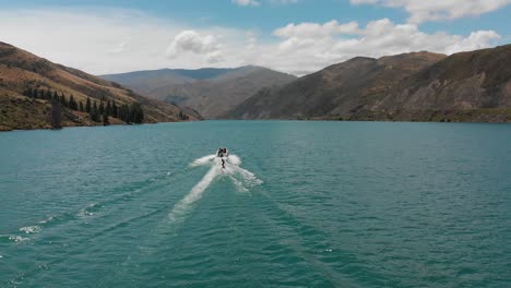 Esquí-Acuático-Detrás-De-Un-Barco-En-El-Lago-Dunstan-Cerca-De-La-Represa-Clyde,-Otago-Central,-Nueva-Zelanda-Con-Montañas-Y-Nubes-En-El-Fondo