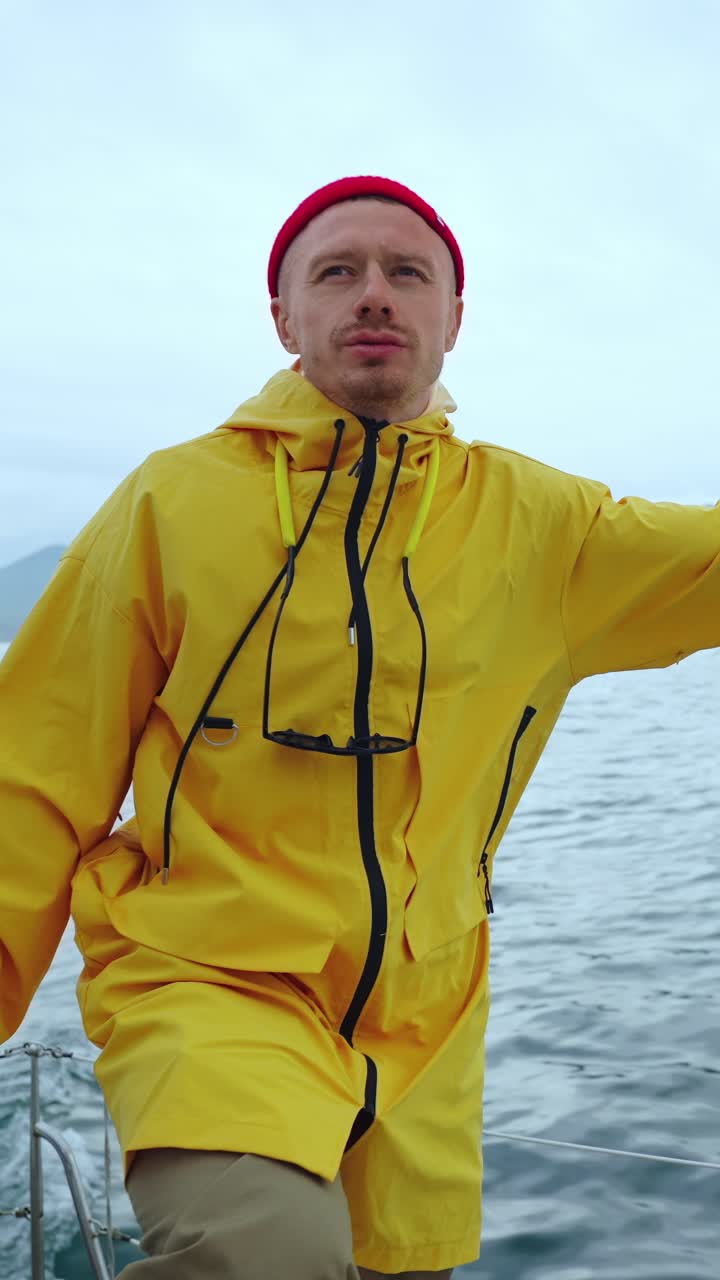 黄色いレインコートと赤いビーニー帽をかぶった男性が海を航海している。