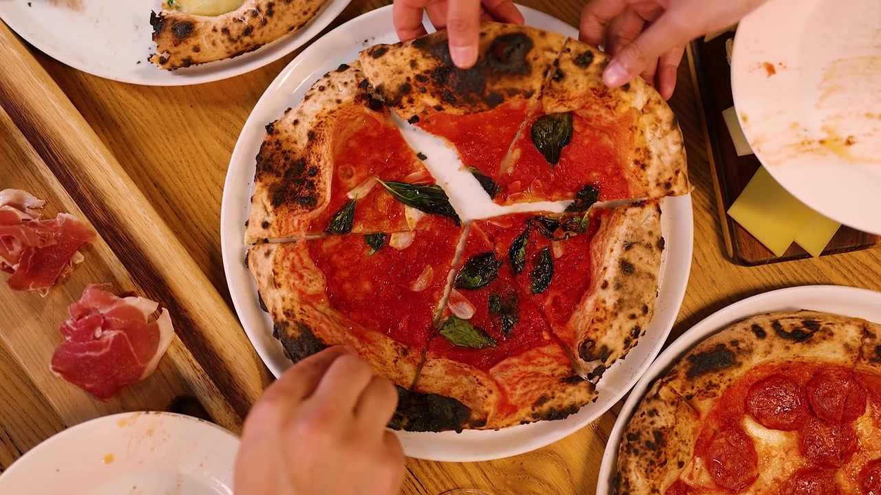 Vista dall'alto di mani che prendono fette di pizza fresca cotta nel forno a legna durante una cena di gruppo.