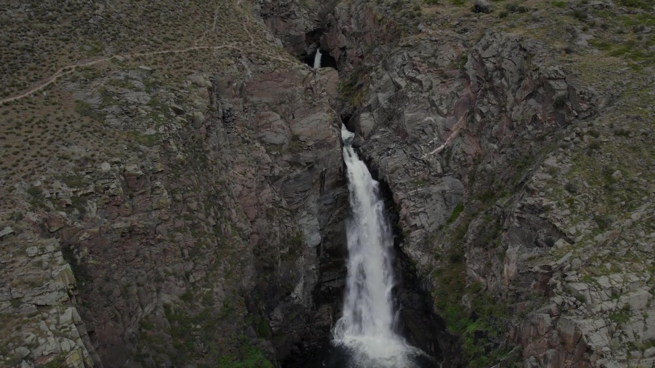 Droneopptak av Kurkure-fossen som stuper ned i en smal steinete canyon, omgitt av ulendte fjellsider og sparsom vegetasjon i Altai, Russland