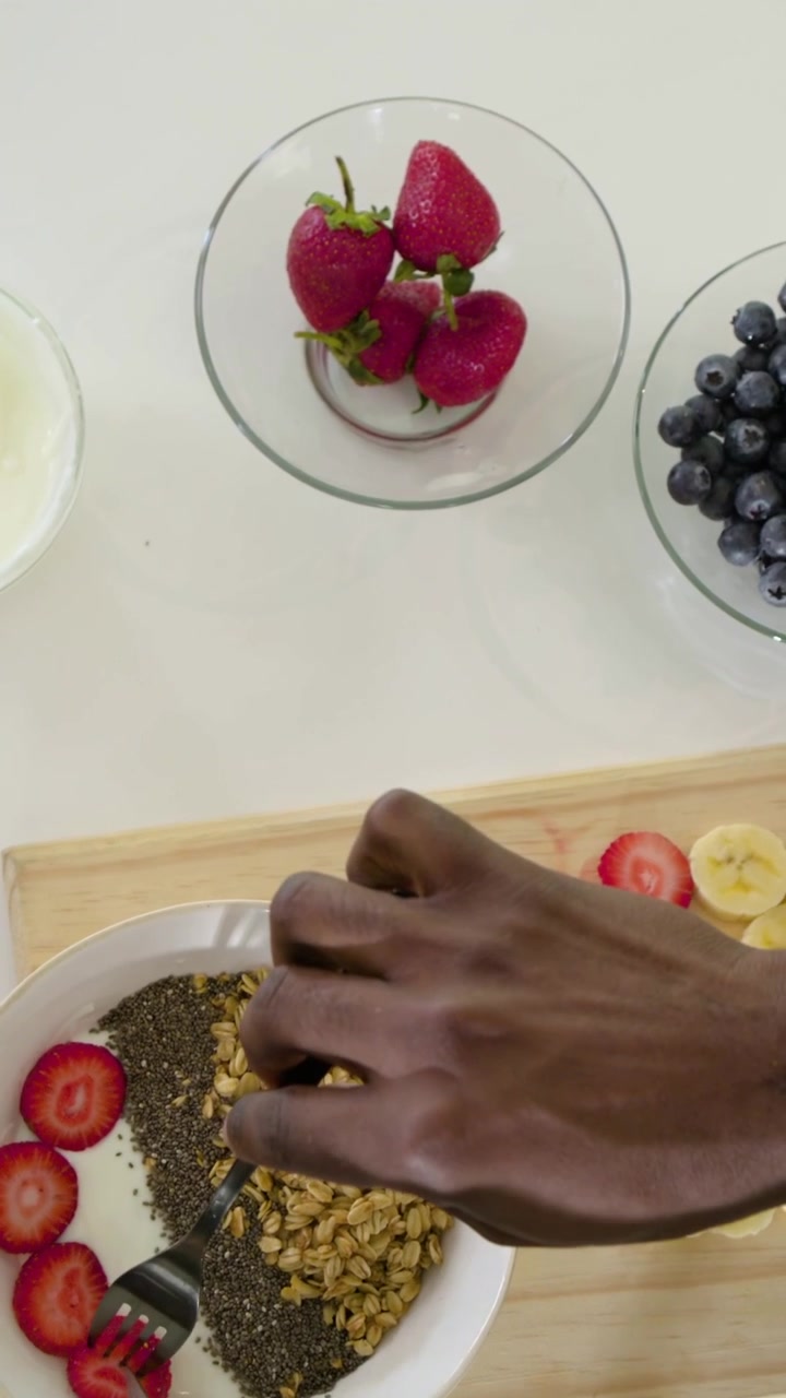Video verticale: Raccogliere fragole, mani che le prendono e le dispongono sullo yogurt a casa per colazione.