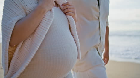 임신한 배를 만지는 남자의 손, 해변을 는 여자의 가까운 모습, 미래의 부모
