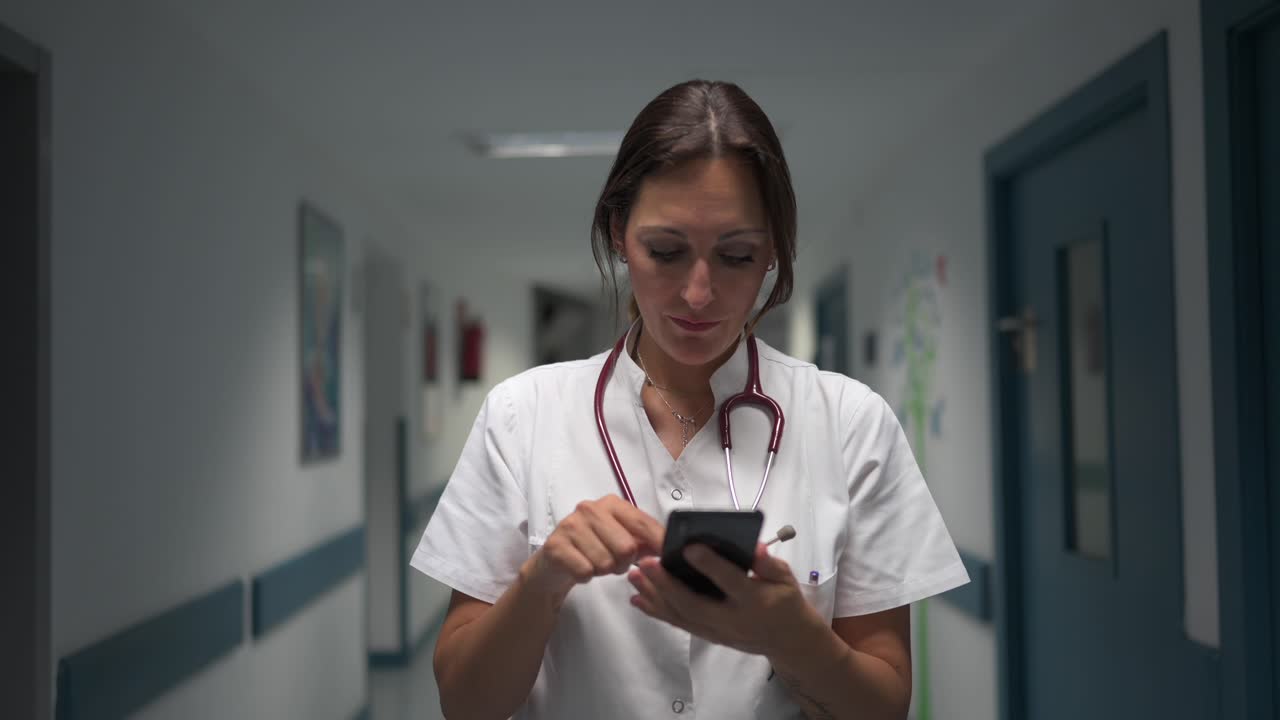 Pediatra alegre usando el smartphone en el pasillo del hospital