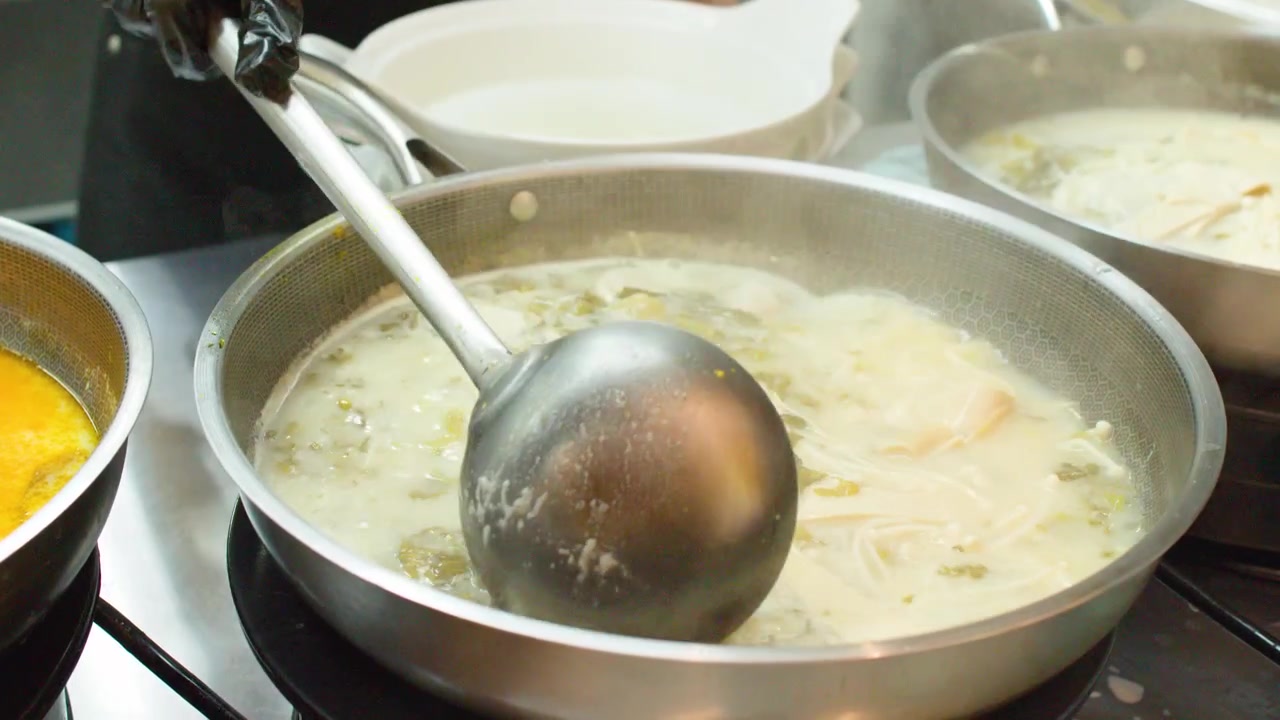 Close-up shot of chef using metal ladle to stir steaming broth in stainless steel wok.