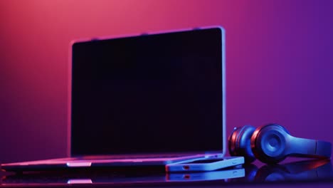 video de computadora portátil, teléfono inteligente y auriculares en el escritorio con espacio de copia en fondo de neón
