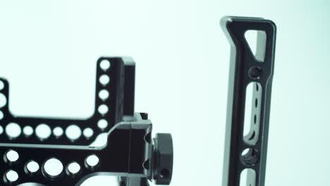 a vertical close up shot of a black metal camera cage with a handler above, video production equipment, on a 360 rotating stand, studio light, slow motion, 4k