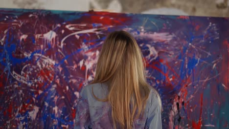 Blonde-woman-reflecting-in-front-her-artwork-in-workshop,-rare-view