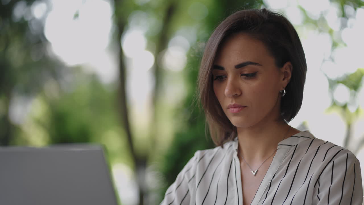 mujer de negocios morena de etnia hispana trabaja remotamente mientras está sentada en un café de verano en un día soleado.