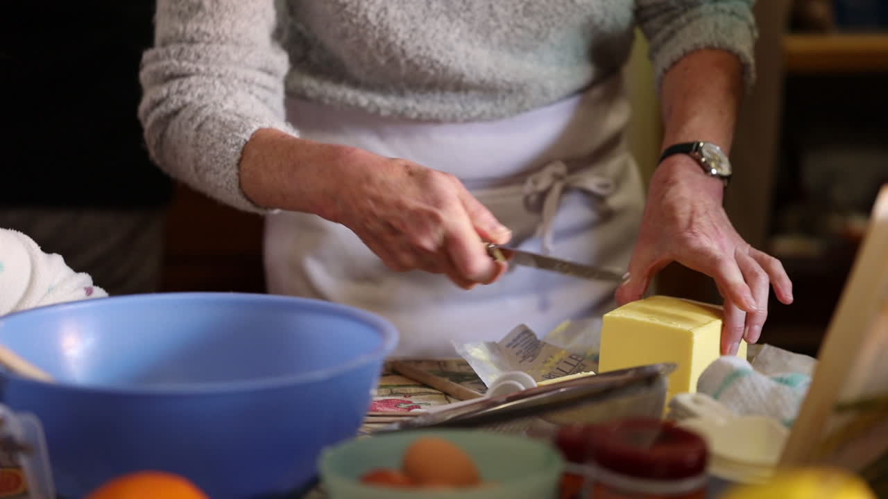 anciana cortando mantequilla mientras hornea en una cocina casera