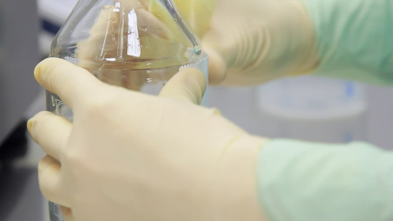 Laboratory worker sticking sticker at bottle with transparent liquid
