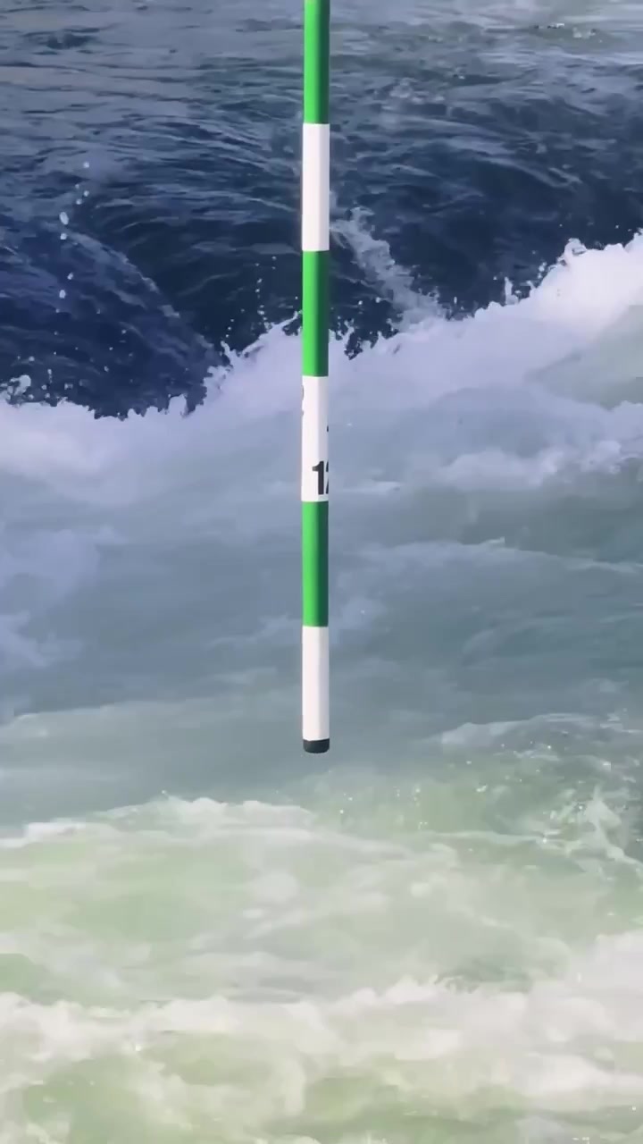 Gros plan vertical d'un piquet de slalom de kayak au-dessus d'eaux vives puissantes sur le parcours de Tacen en Slovénie, avec des rapides bleu-vert, de l'écume et un courant rapide.
