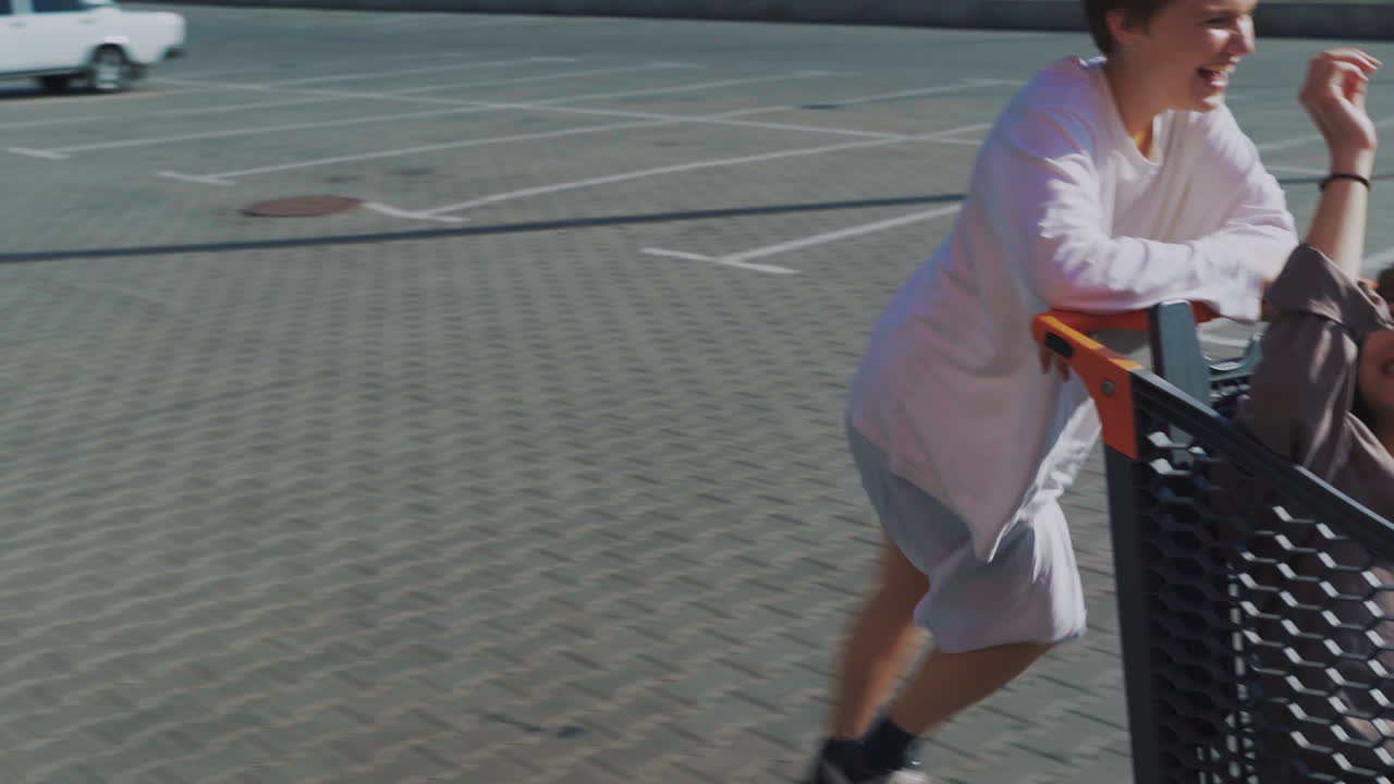 dos mujeres divirtiéndose empujando el carrito de compras en el estacionamiento