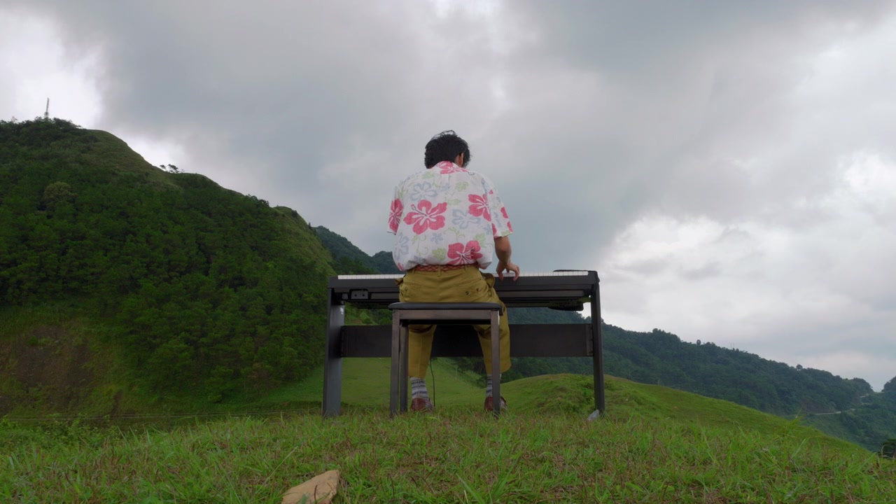山の尾根でピアノを弾くビンテージなアジア人男性ミュージシャンの後ろ姿。
