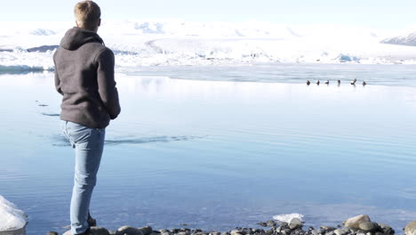 young male traveler skipping stones in beautiful glacial lagoon in iceland in slow motion