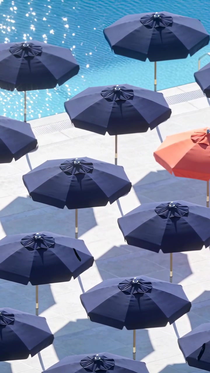 Video verticale: Telecamera che si muove lentamente mostrando una griglia di ombrelloni blu scuro accanto a una piscina turchese