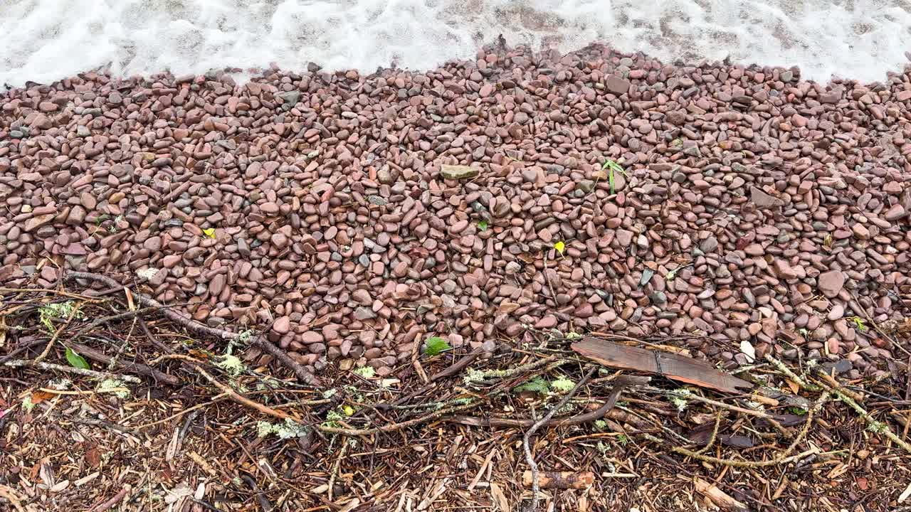 Gentle waves roll onto a rocky pebble beach, overcast lighting, static overhead camera view