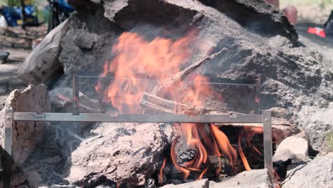 someone tosses firewood on the side of a large open-air bonfire. camping, outdoor recreation and campfire cooking concept, 4k