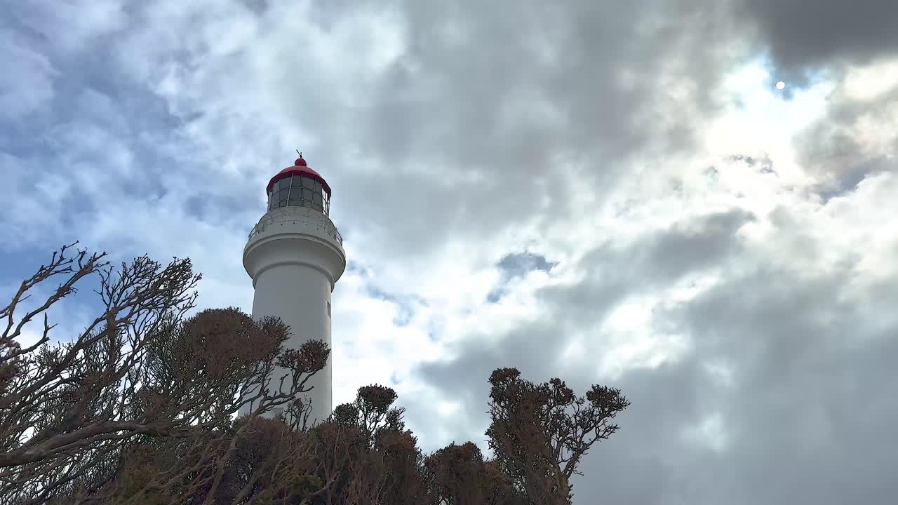 A lighthouse stands tall against a cloudy sky, surrounded by coastal vegetation. Captured with dynamic lighting and a serene atmosphere