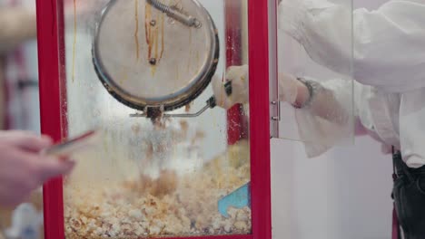 fresh popcorn bursts in a red vintage machine as an attendant scoops it up, a classic snack in the making