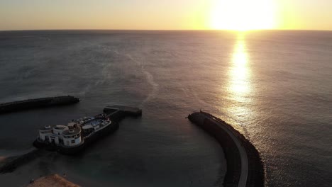 Aerial-View-Of-Golden-Yellow-Sunset-Over-The-Ocean-On-The-Horizon-With-Silhouette-View-Bikini-Beach-Club