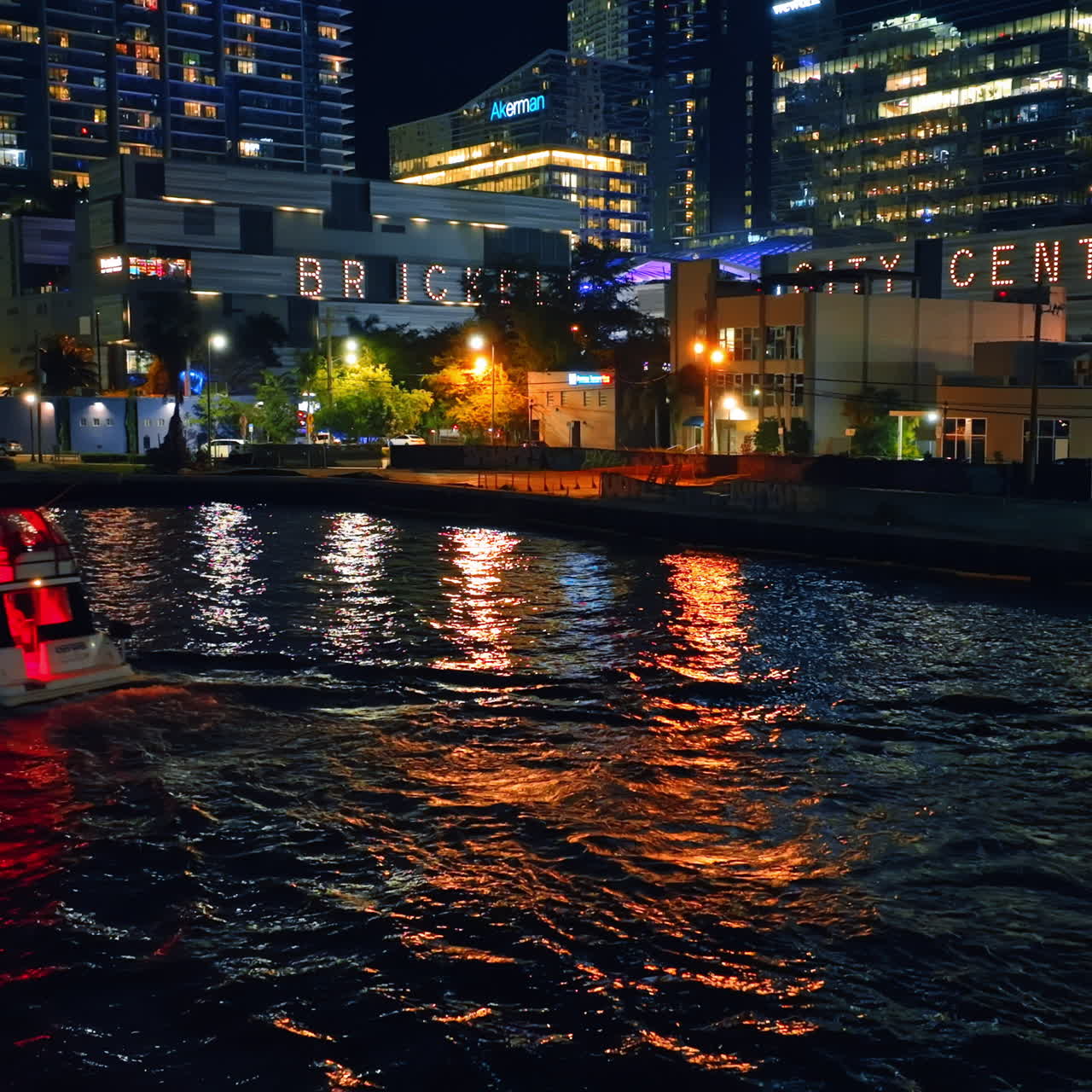 Motor boat going by the river at night. Buildings full of lights on the waterfront of Miami, Florida, USA.