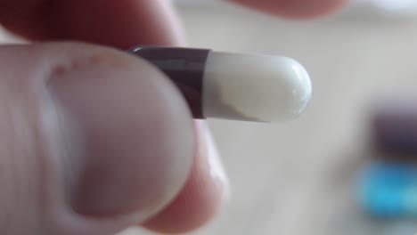 very close-up of a woman's hand holding a capsule between its two fingers and twirling it around