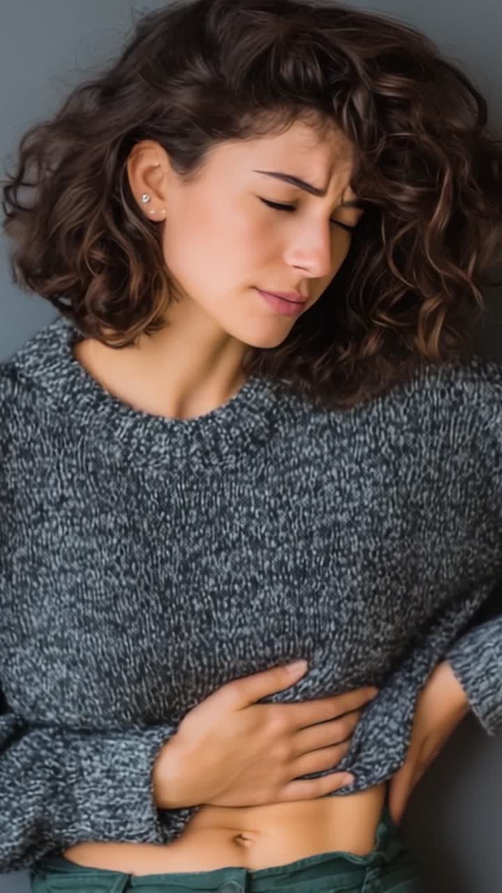 Una donna che prova disagio mentre si tiene lo stomaco, catturata in due fotogrammi che mostrano tensione emotiva e fisica attraverso espressioni e linguaggio del corpo