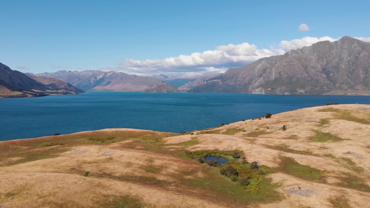 toma aérea de un hermoso lago azul escondido detrás de las colinas cubiertas de hierba en nueva zelanda en un día soleado de verano en 4k