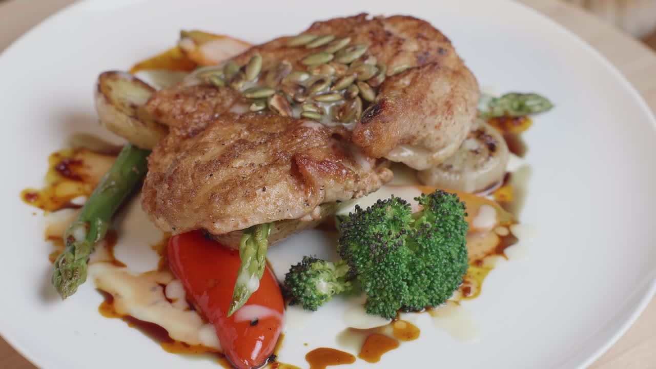 una chuleta de pollo bien presentada, perfectamente chamuscada y asada, cubierta con semillas de calabaza y colocada encima de coloridas verduras