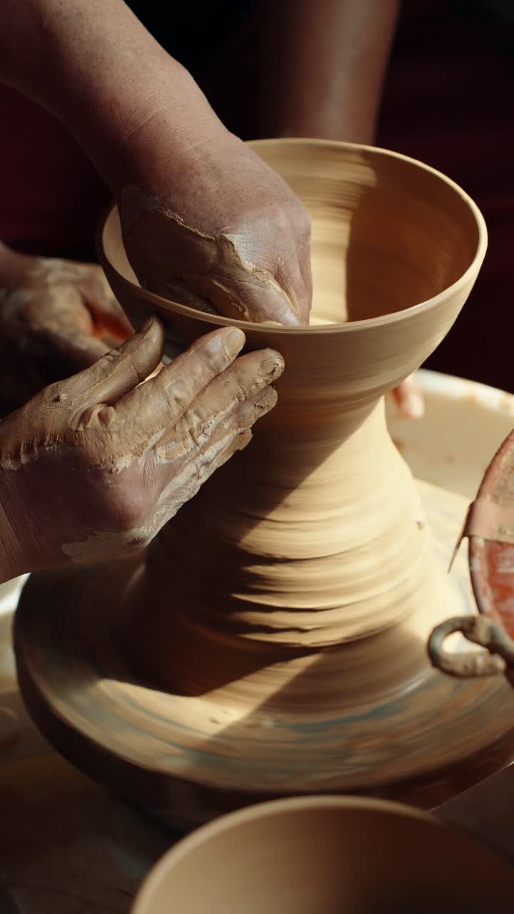 Un primo piano mostra un vasaio esperto che insegna e guida le mani di uno studente a modellare un vaso dall'argilla bagnata su un tornio da vasaio che gira durante una lezione d'arte