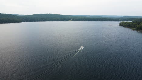 Rear-view-slow-motion-tracking-boat-and-wake-cruising-through-wide-open-lake,-diffused-light-cuts-through-cloud