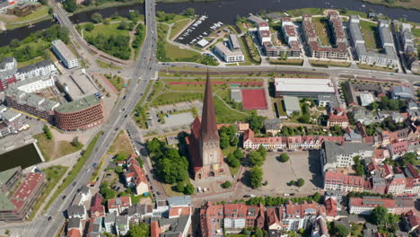 Aerial-view-of-Saint-Peters-church-with-tall-pointed-tower.-Backwards-and-tilt-up-reveal-of-surrounding-buildings-in-town