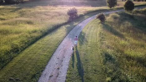 Older-white-male-running-on-a-gravel-driveway-surrounded-with-greenery-and-being-followed-by-a-husky-dog-at-sunset