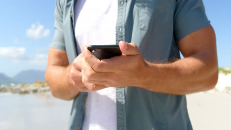 Mittelteil-Eines-Mannes,-Der-An-Einem-Sonnigen-Tag-Am-Strand-Sein-Mobiltelefon-Benutzt,-4k