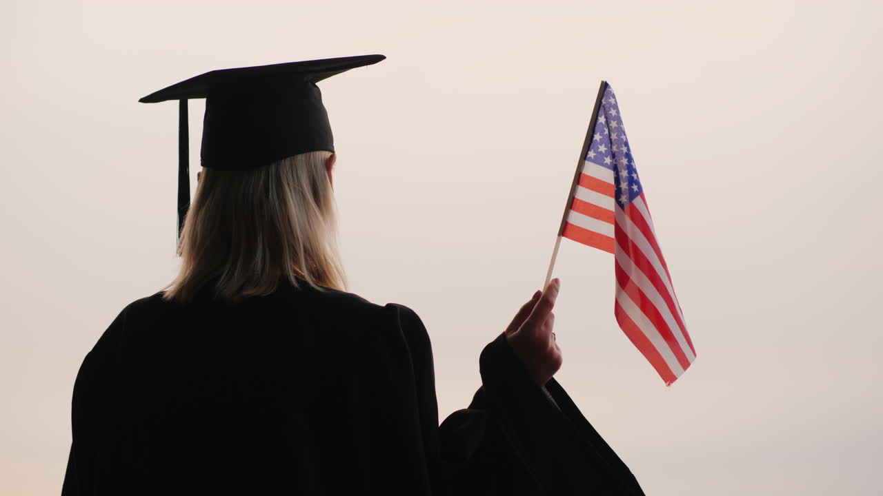 estudiante en uniforme de posgrado con bandera de estados unidos en la mano