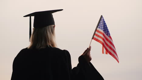 Estudiante-En-Uniforme-De-Posgrado-Con-Bandera-De-Estados-Unidos-En-La-Mano